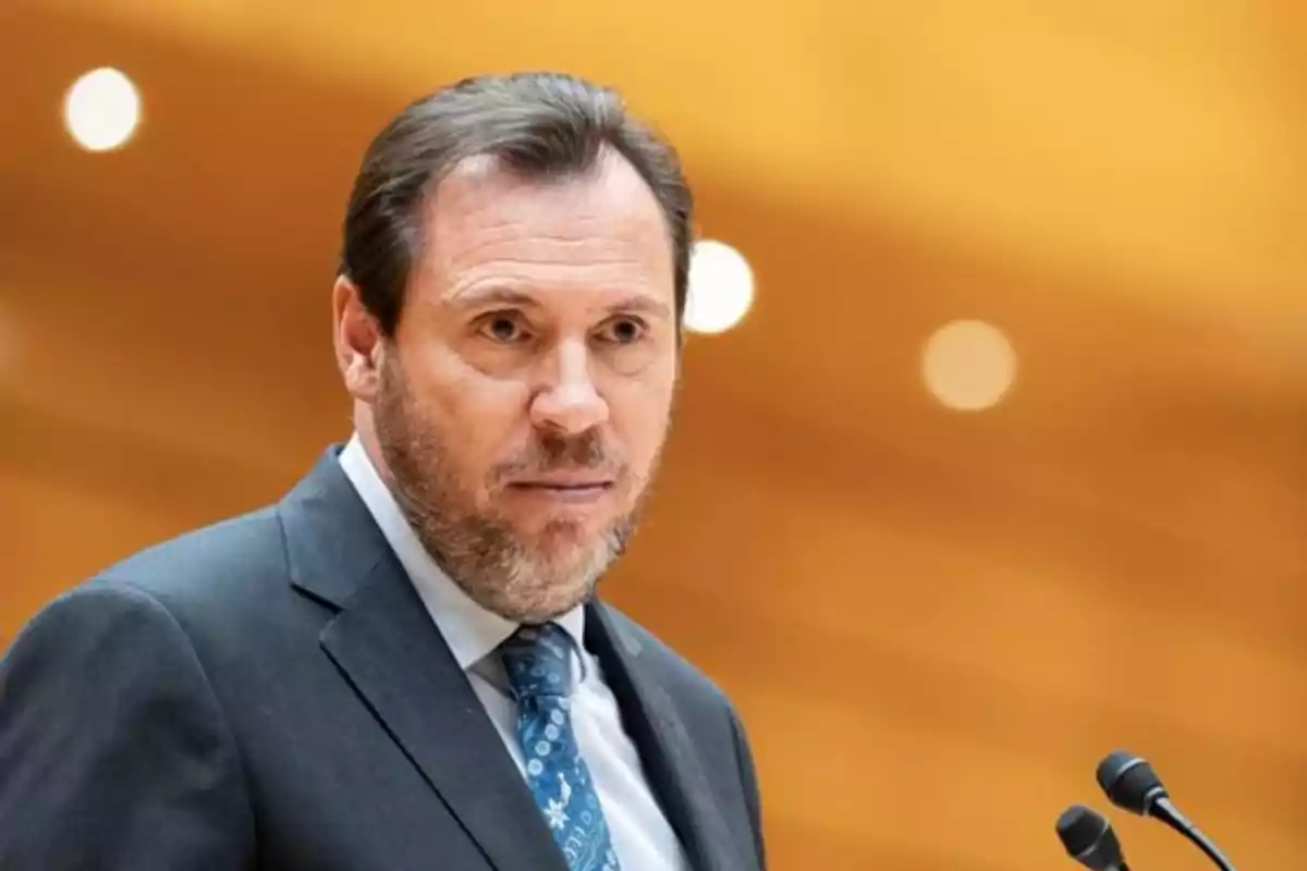 Hombre de traje y corbata hablando frente a un micrófono con fondo desenfocado de tonos cálidos Hombre de traje y corbata hablando frente a un micrófono con fondo desenfocado de tonos cálidos