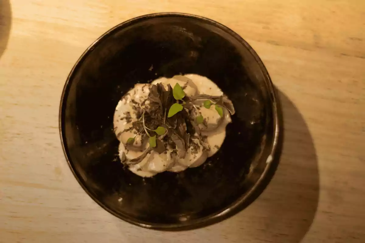 Plato negro con un postre cremoso decorado con hojas verdes y virutas de chocolate sobre una mesa de madera clara Plato negro con un postre cremoso decorado con hojas verdes y virutas de chocolate sobre una mesa de madera clara