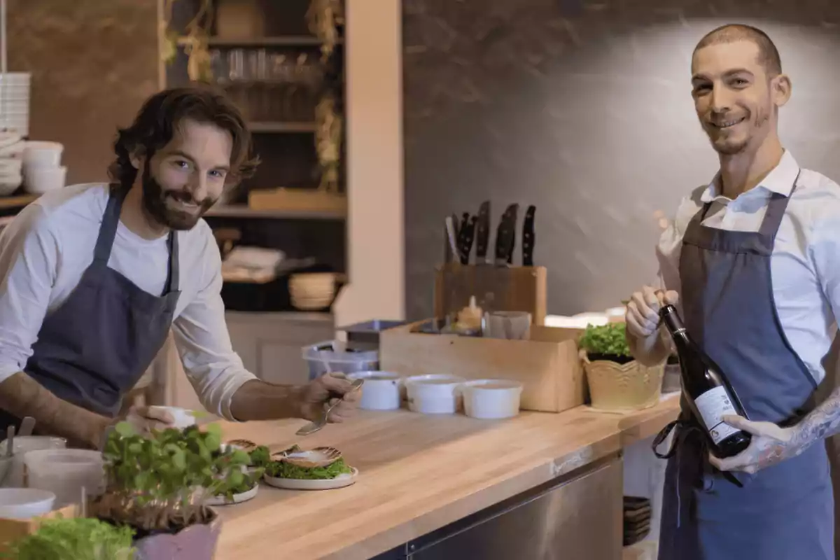 Dos cocineros sonrientes en una cocina moderna, uno sirviendo comida en platos y el otro sosteniendo una botella de vino Dos cocineros sonrientes en una cocina moderna, uno sirviendo comida en platos y el otro sosteniendo una botella de vino