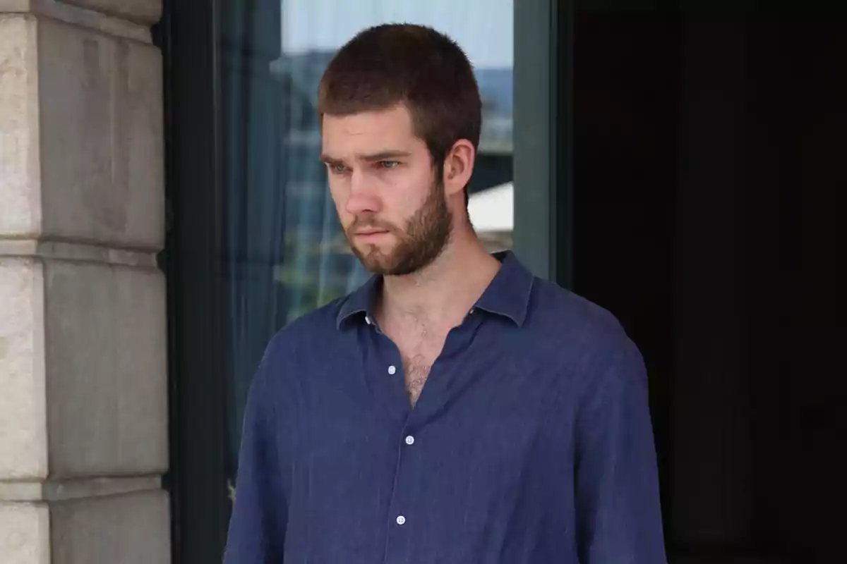 Young man with a beard and short hair is wearing a blue jersey and standing in front of a glass door with a serious expression. Young man with a beard and short hair is wearing a blue jersey and standing in front of a glass door with a serious expression.