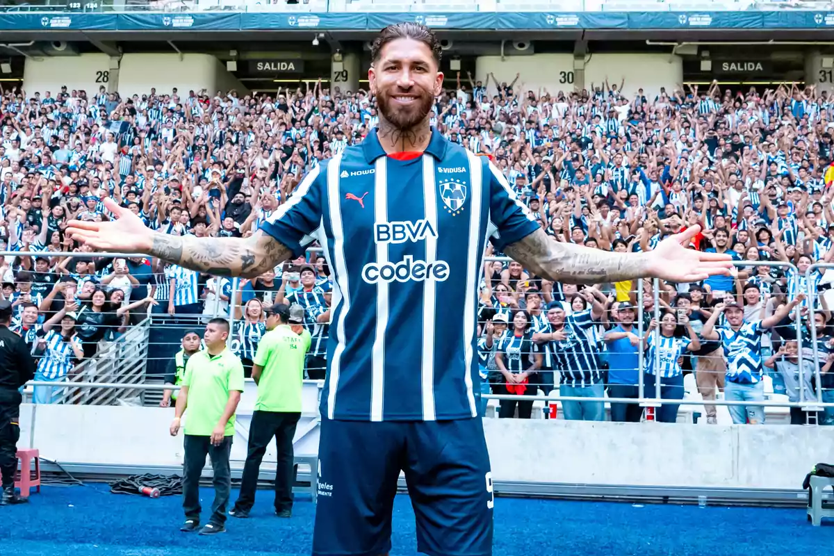 Futbolista con uniforme de Rayados de Monterrey sonríe con los brazos abiertos frente a una multitud de aficionados en el estadio Futbolista con uniforme de Rayados de Monterrey sonríe con los brazos abiertos frente a una multitud de aficionados en el estadio