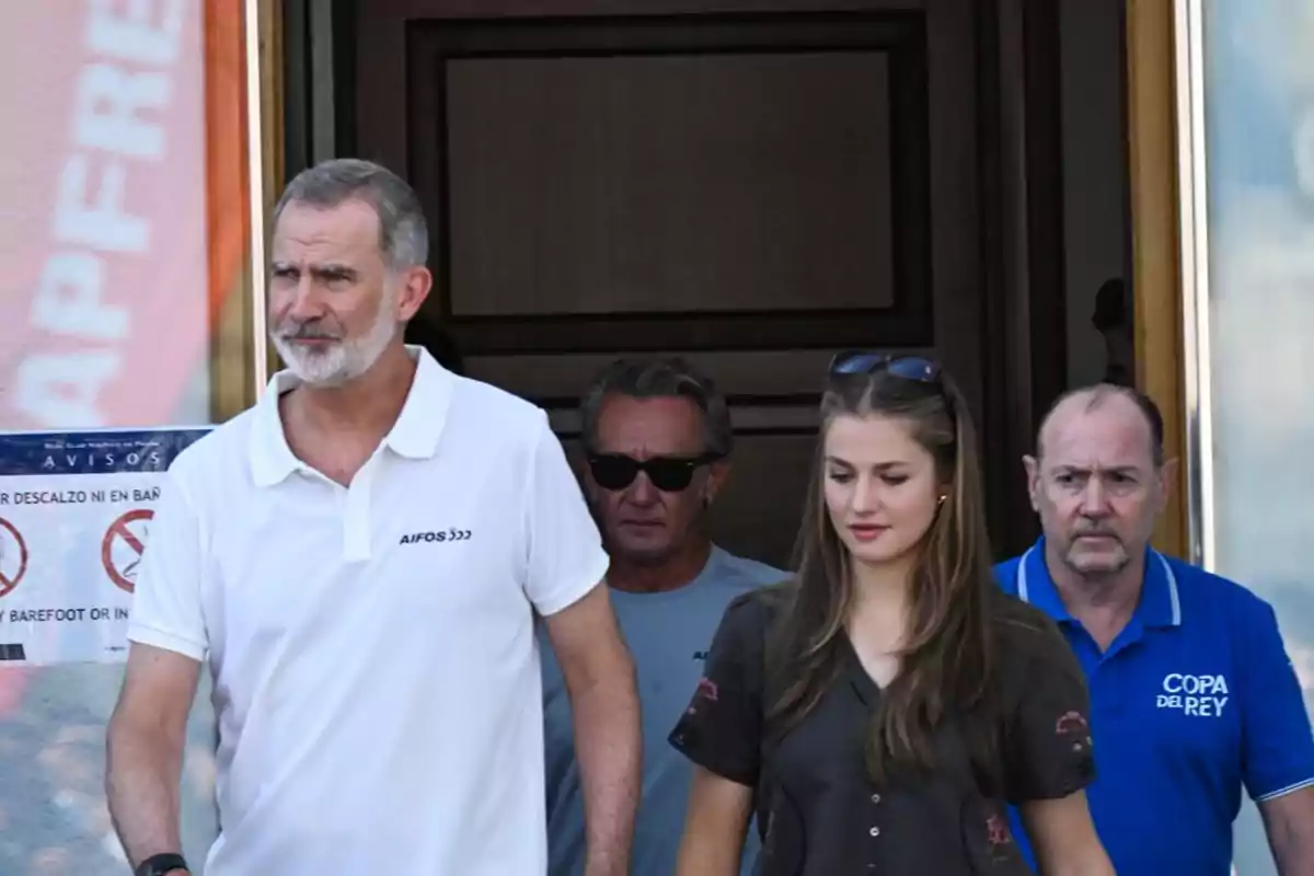 Un hombre de barba con camiseta blanca y una joven de cabello largo caminan juntos acompañados de dos hombres mayores uno con gafas de sol y otro con polo azul