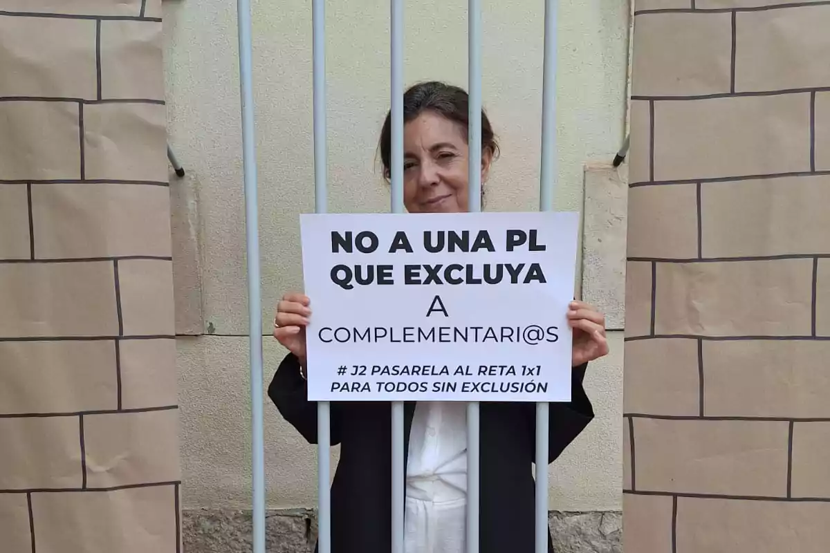 Mujer detrás de unas barras simulando estar en una cárcel, sosteniendo un cartel que protesta contra la exclusión de los complementarios en una propuesta de ley Mujer detrás de unas barras simulando estar en una cárcel, sosteniendo un cartel que protesta contra la exclusión de los complementarios en una propuesta de ley