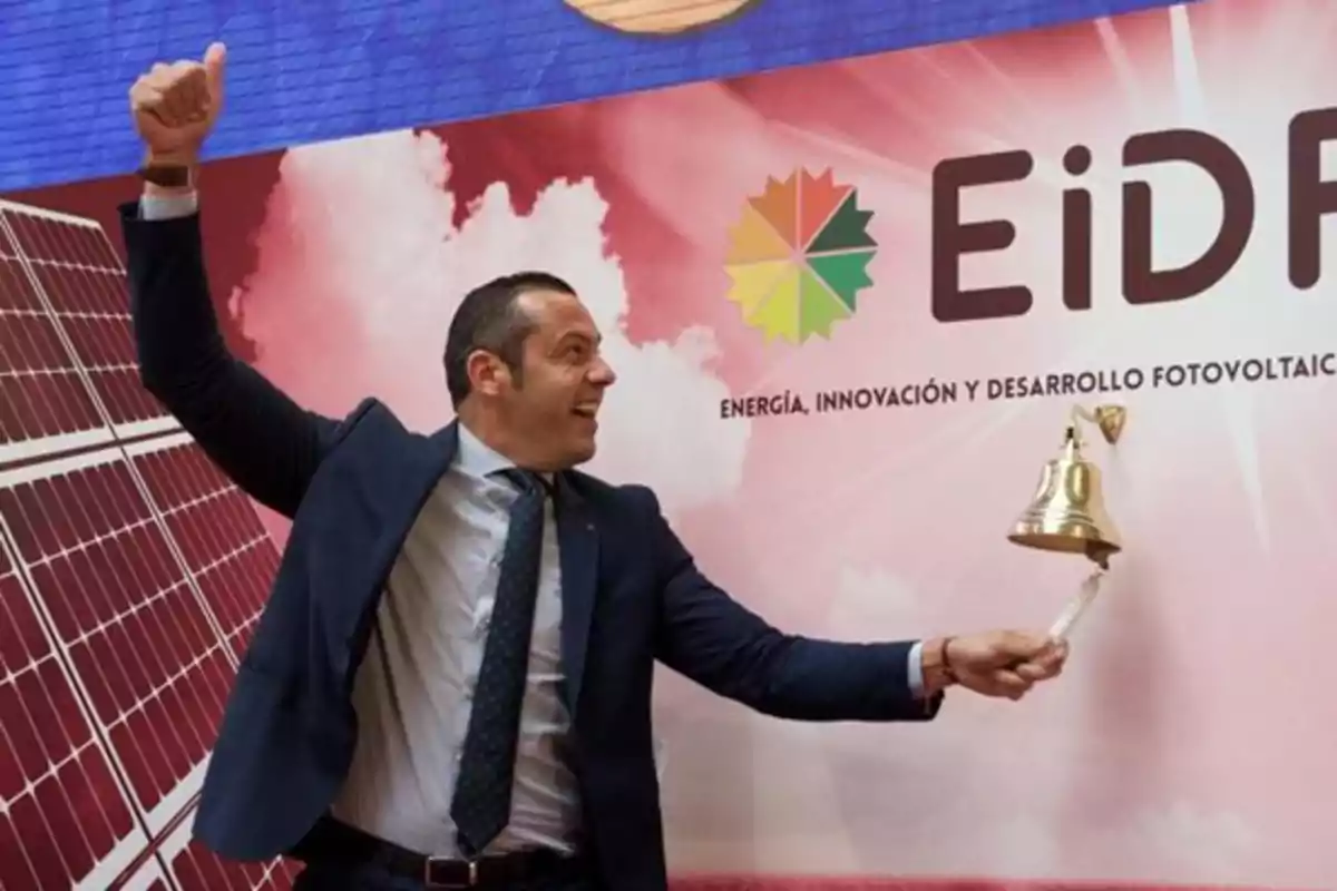 Hombre de traje tocando una campana frente a un cartel de una empresa de energía solar Hombre de traje tocando una campana frente a un cartel de una empresa de energía solar