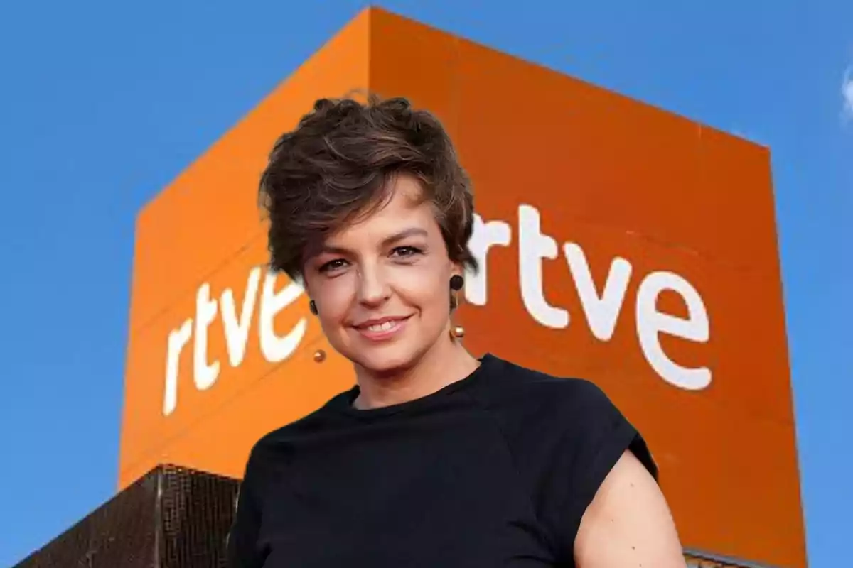 Mujer de cabello corto y oscuro sonriendo frente a un edificio naranja con el logo de rtve sobre un cielo azul