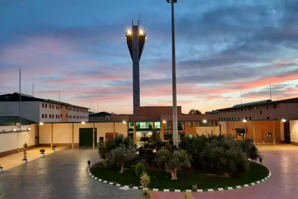 Edificio con torre de vigilancia al atardecer rodeado de jardines y caminos pavimentados Edificio con torre de vigilancia al atardecer rodeado de jardines y caminos pavimentados