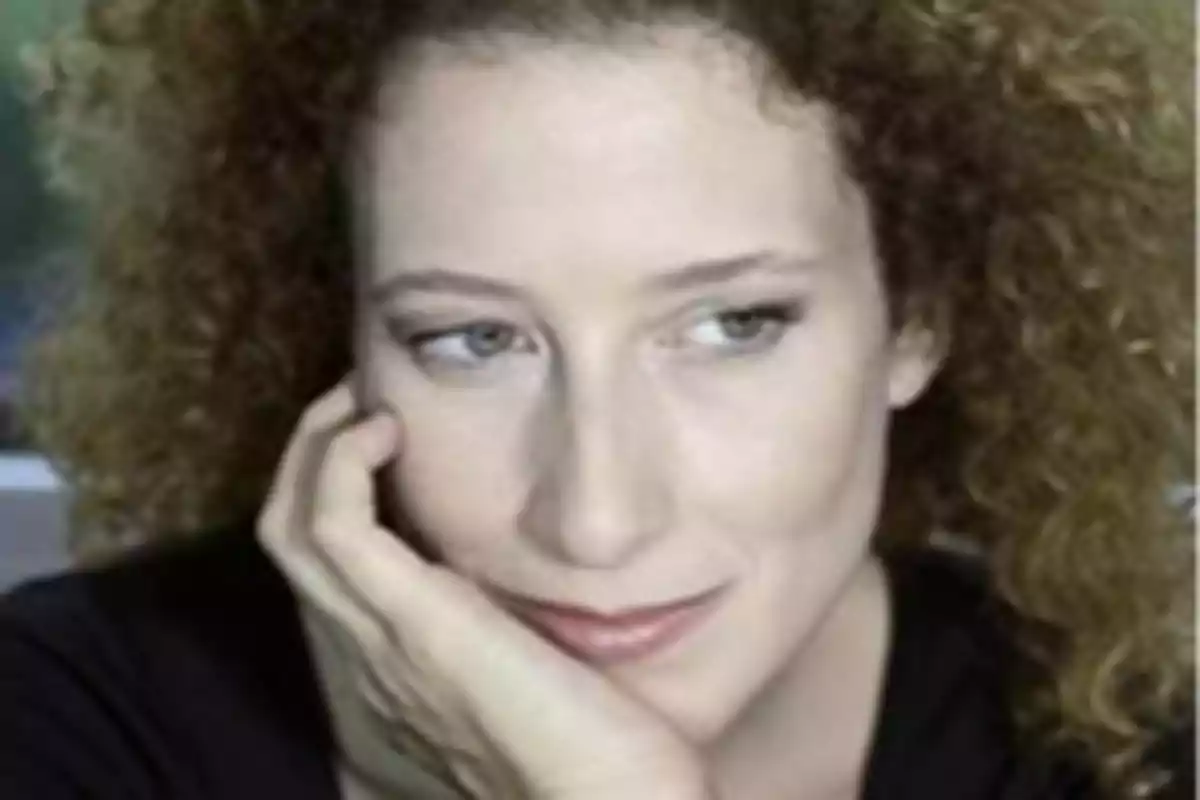 Mujer de cabello rizado y rubio apoyando su rostro en una mano mientras mira hacia un lado Mujer de cabello rizado y rubio apoyando su rostro en una mano mientras mira hacia un lado