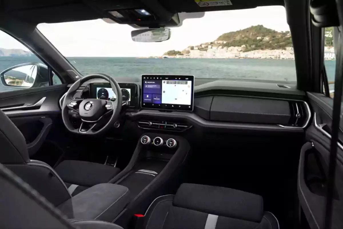 Interior moderno de un automóvil con volante multifunción, pantallas digitales y vista al mar a través del parabrisas Interior moderno de un automóvil con volante multifunción, pantallas digitales y vista al mar a través del parabrisas
