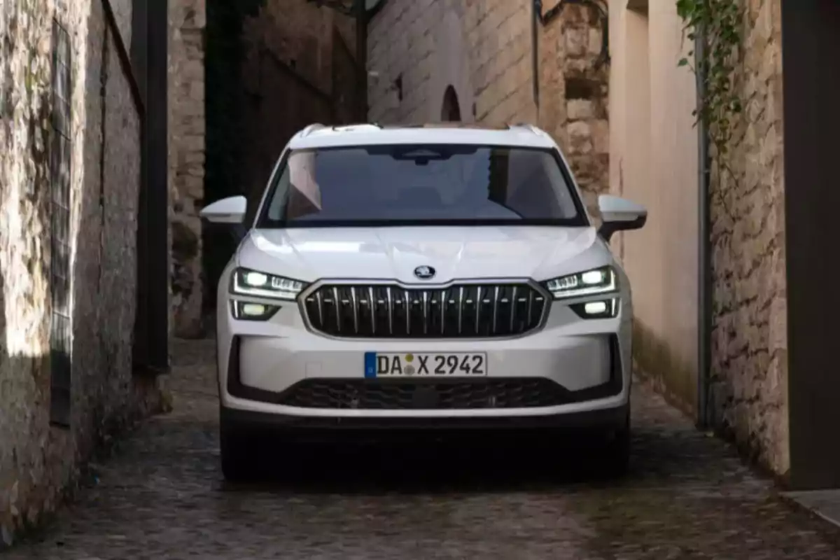 Un SUV blanco circula por una calle angosta de piedra entre paredes de edificios antiguos. Un SUV blanco circula por una calle angosta de piedra entre paredes de edificios antiguos.