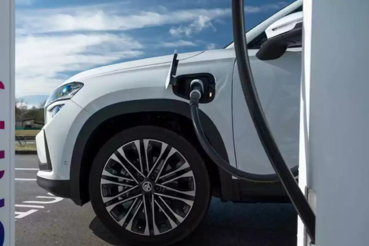 Automóvil blanco conectado a una estación de carga eléctrica bajo un cielo parcialmente nublado Automóvil blanco conectado a una estación de carga eléctrica bajo un cielo parcialmente nublado