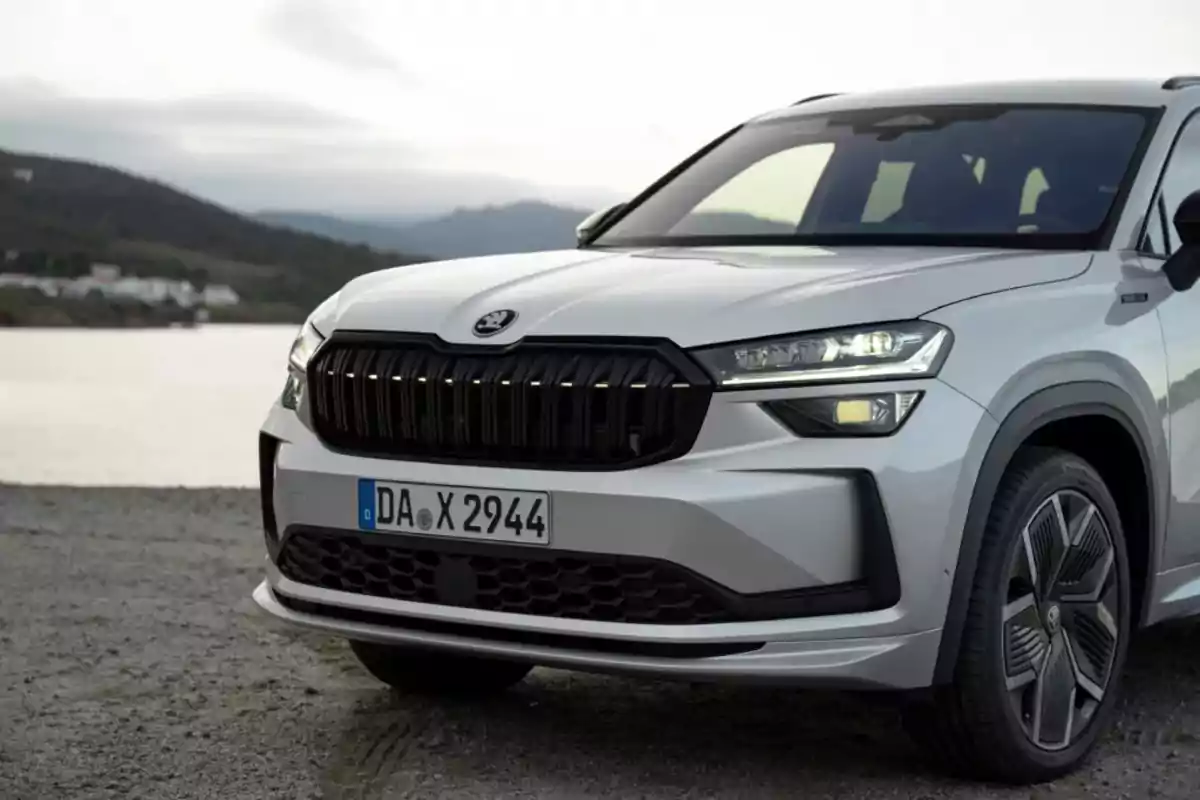 Frontal de un coche SUV blanco estacionado junto a un lago con montañas al fondo Frontal de un coche SUV blanco estacionado junto a un lago con montañas al fondo