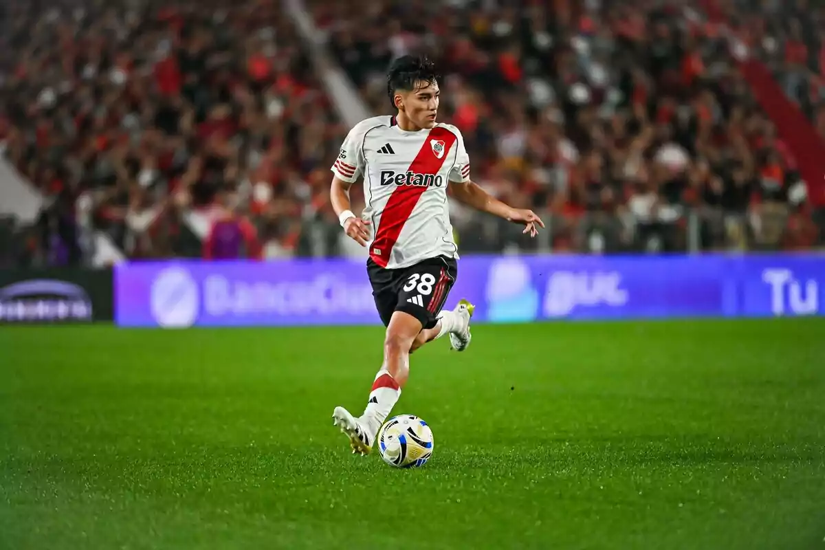 Jugador de River Plate con el número 38 en la camiseta corre con el balón en un estadio lleno de espectadores