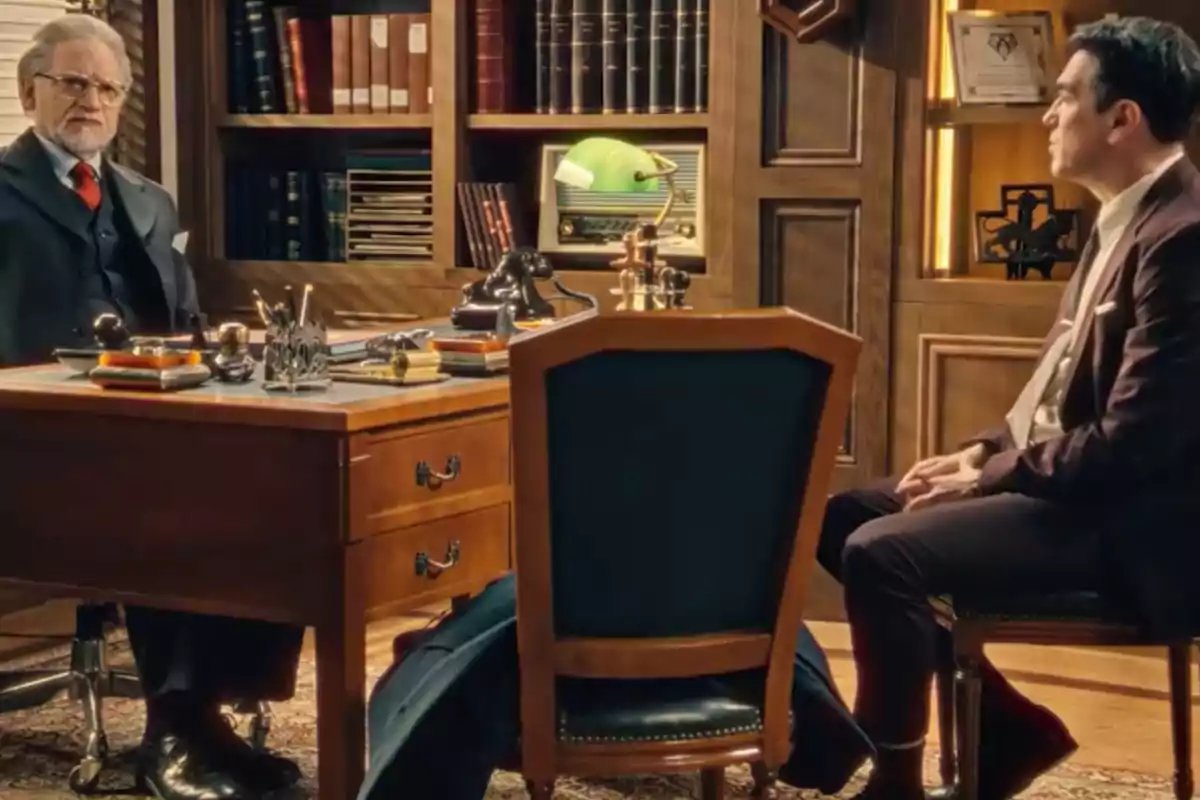 Damián y Gabriel elegantemente vestidos conversan en una oficina con muebles de madera y estanterías llenas de libros. Captura de 'Sueños de libertad' Damián y Gabriel elegantemente vestidos conversan en una oficina con muebles de madera y estanterías llenas de libros. Captura de 'Sueños de libertad'