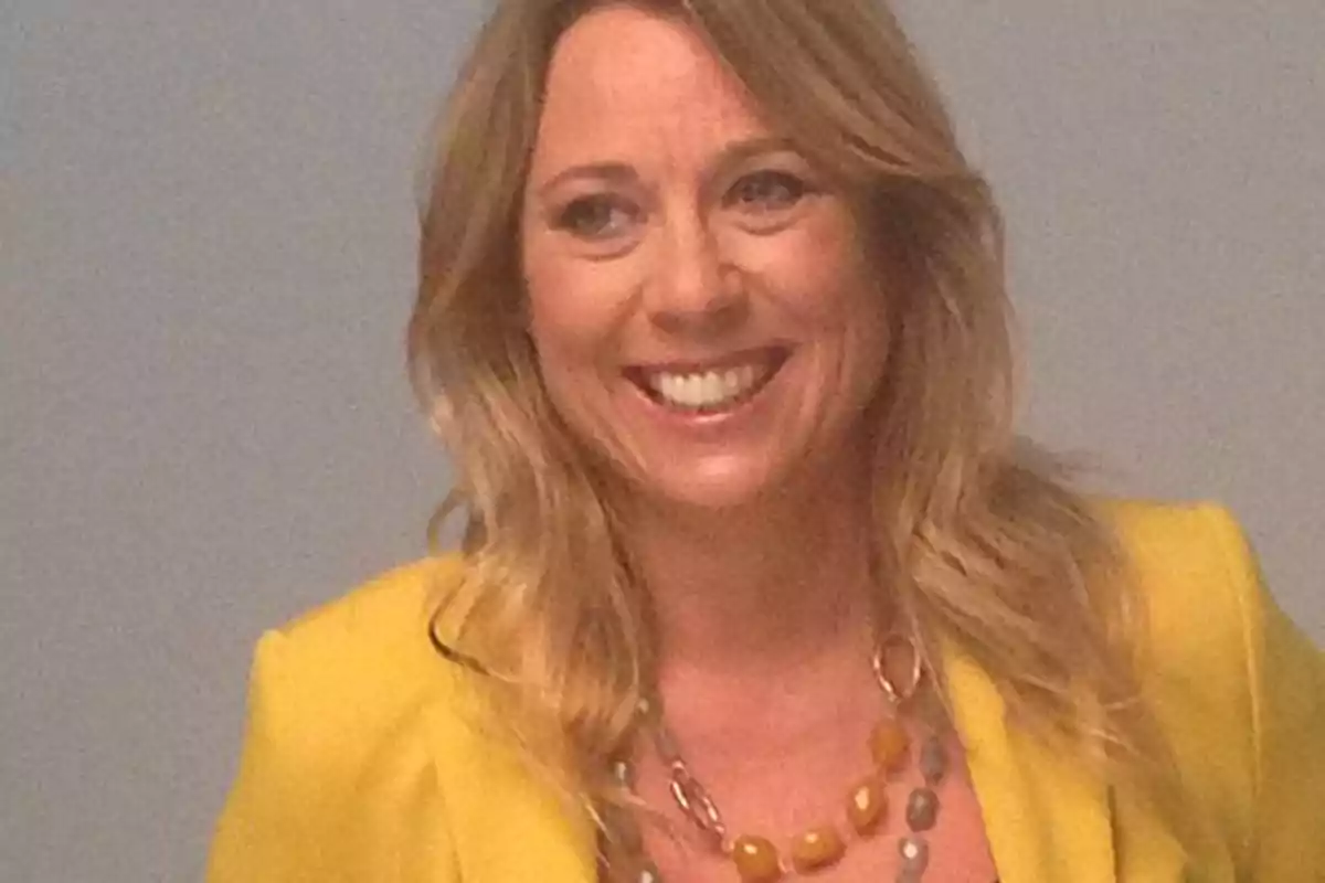 Mujer rubia sonriendo con chaqueta amarilla y collar de cuentas Mujer rubia sonriendo con chaqueta amarilla y collar de cuentas