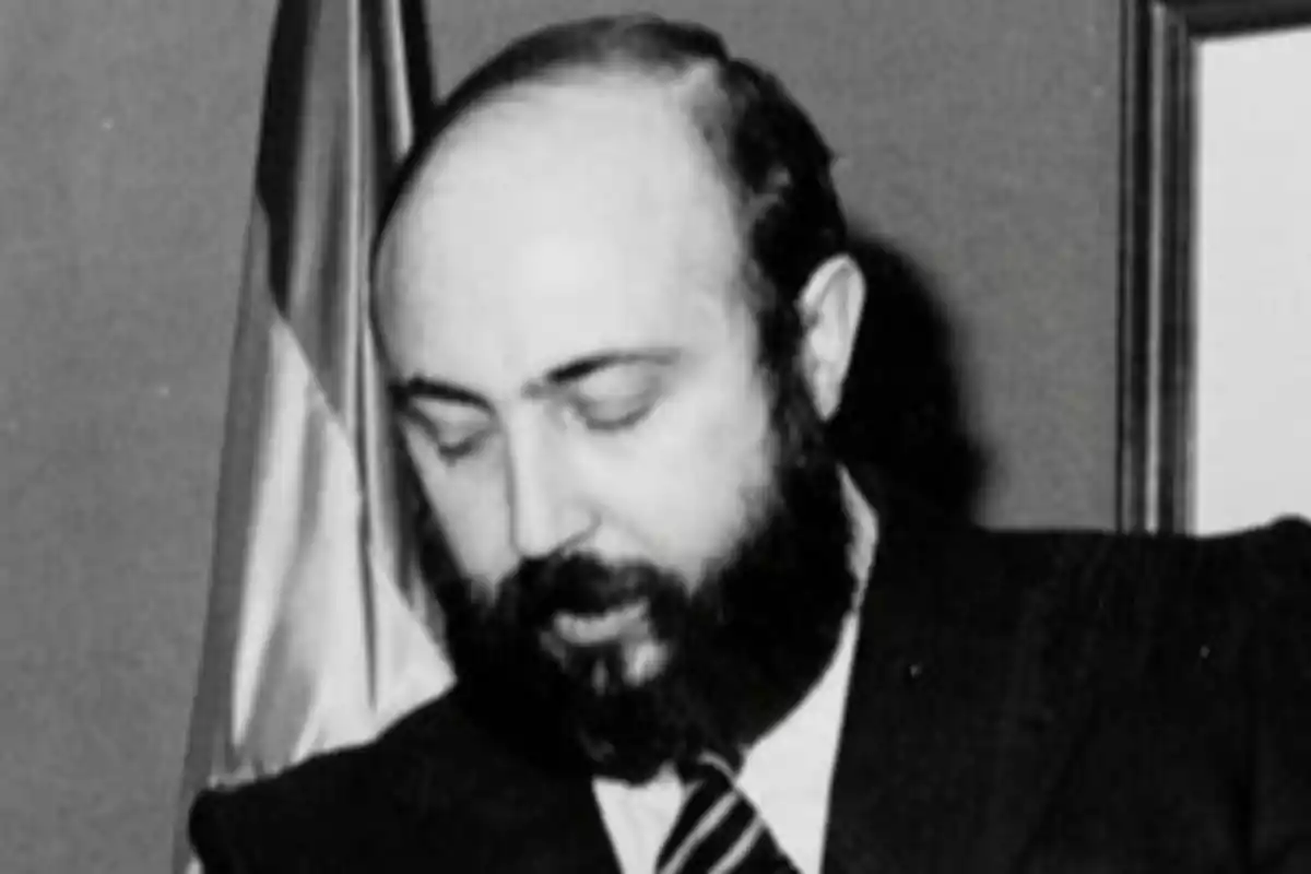 Hombre de mediana edad con barba y traje oscuro mirando hacia abajo en una fotografía en blanco y negro Hombre de mediana edad con barba y traje oscuro mirando hacia abajo en una fotografía en blanco y negro