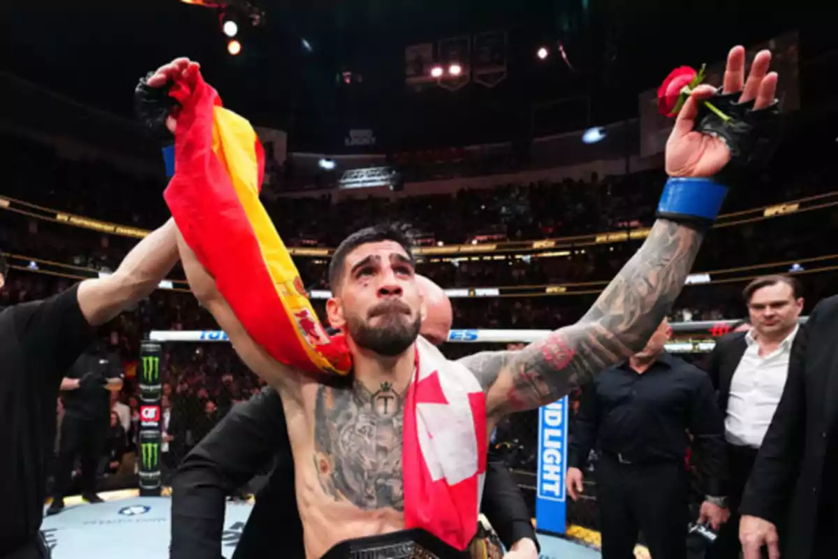 Peleador de artes marciales mixtas celebrando una victoria en el octágono con una bandera de España y una rosa roja en la mano mientras el público lo observa Peleador de artes marciales mixtas celebrando una victoria en el octágono con una bandera de España y una rosa roja en la mano mientras el público lo observa