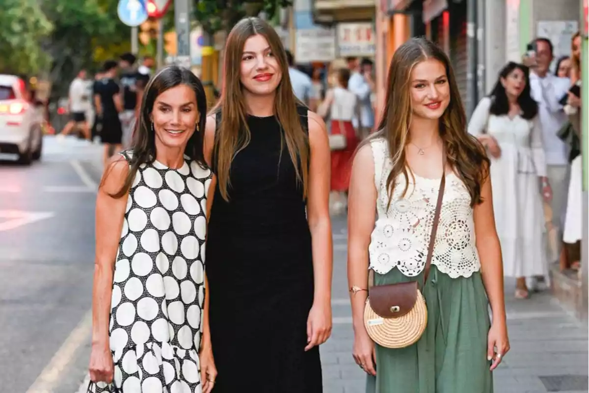 Tres mujeres sonríen mientras caminan por una calle peatonal concurrida, una lleva un vestido blanco con círculos negros, otra un vestido negro y la tercera un top blanco de crochet con falda verde y bolso redondo. Tres mujeres sonríen mientras caminan por una calle peatonal concurrida, una lleva un vestido blanco con círculos negros, otra un vestido negro y la tercera un top blanco de crochet con falda verde y bolso redondo.