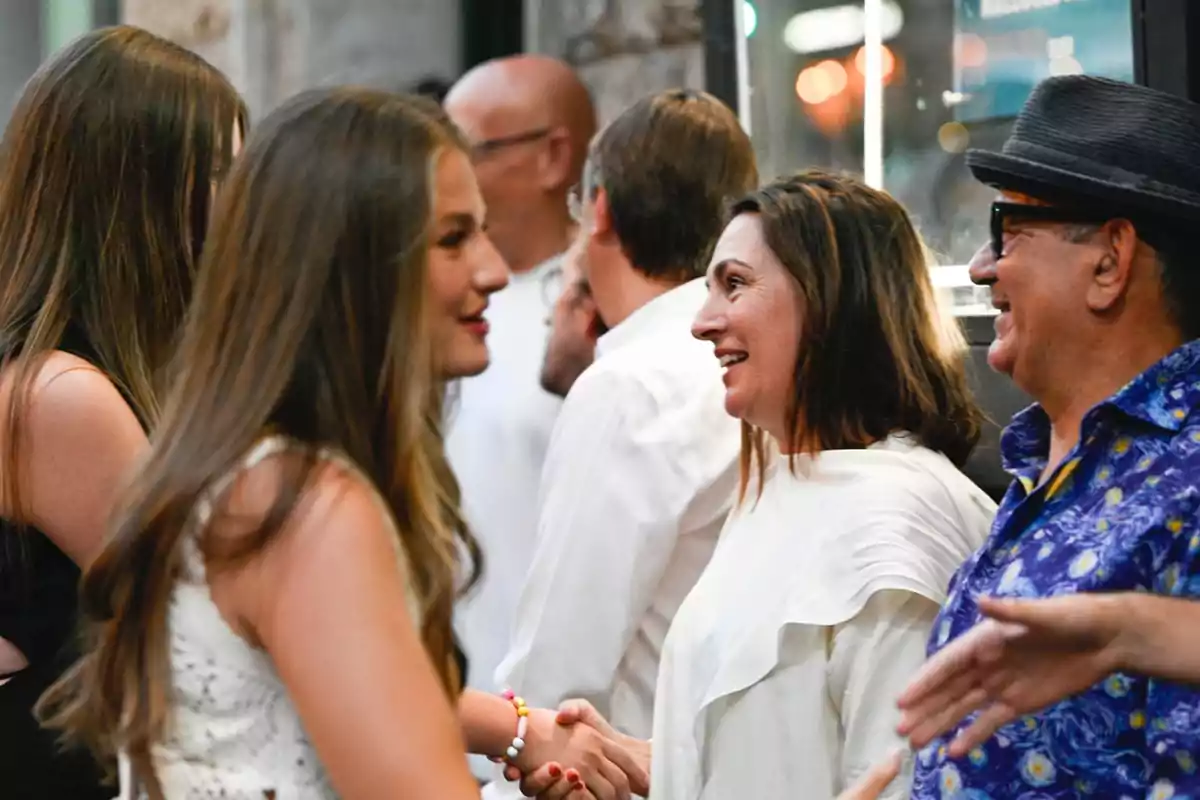 Varias personas sonríen y conversan mientras se saludan de mano en un ambiente social relajado Varias personas sonríen y conversan mientras se saludan de mano en un ambiente social relajado