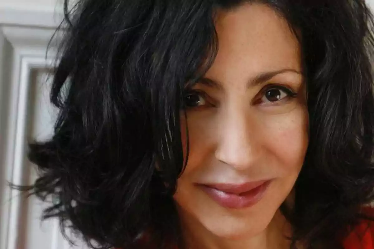 Mujer de cabello oscuro y ondulado mirando a la cámara con una expresión amigable Mujer de cabello oscuro y ondulado mirando a la cámara con una expresión amigable