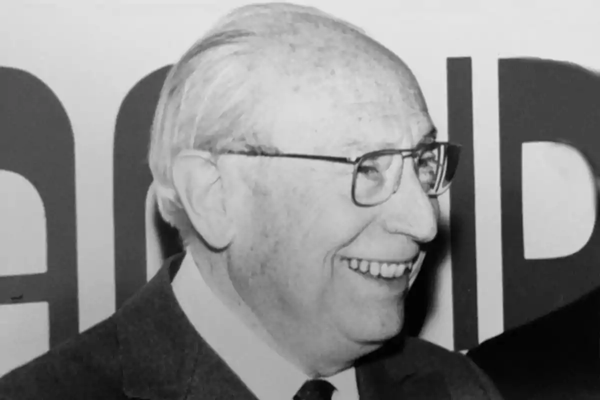 Hombre mayor de perfil sonriendo, usando gafas y traje, en una fotografía en blanco y negro Hombre mayor de perfil sonriendo, usando gafas y traje, en una fotografía en blanco y negro