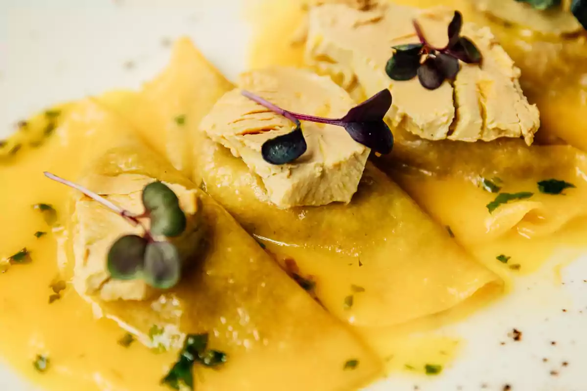Ravioles gourmet cubiertos con foie gras y brotes frescos sobre salsa cremosa amarilla Ravioles gourmet cubiertos con foie gras y brotes frescos sobre salsa cremosa amarilla