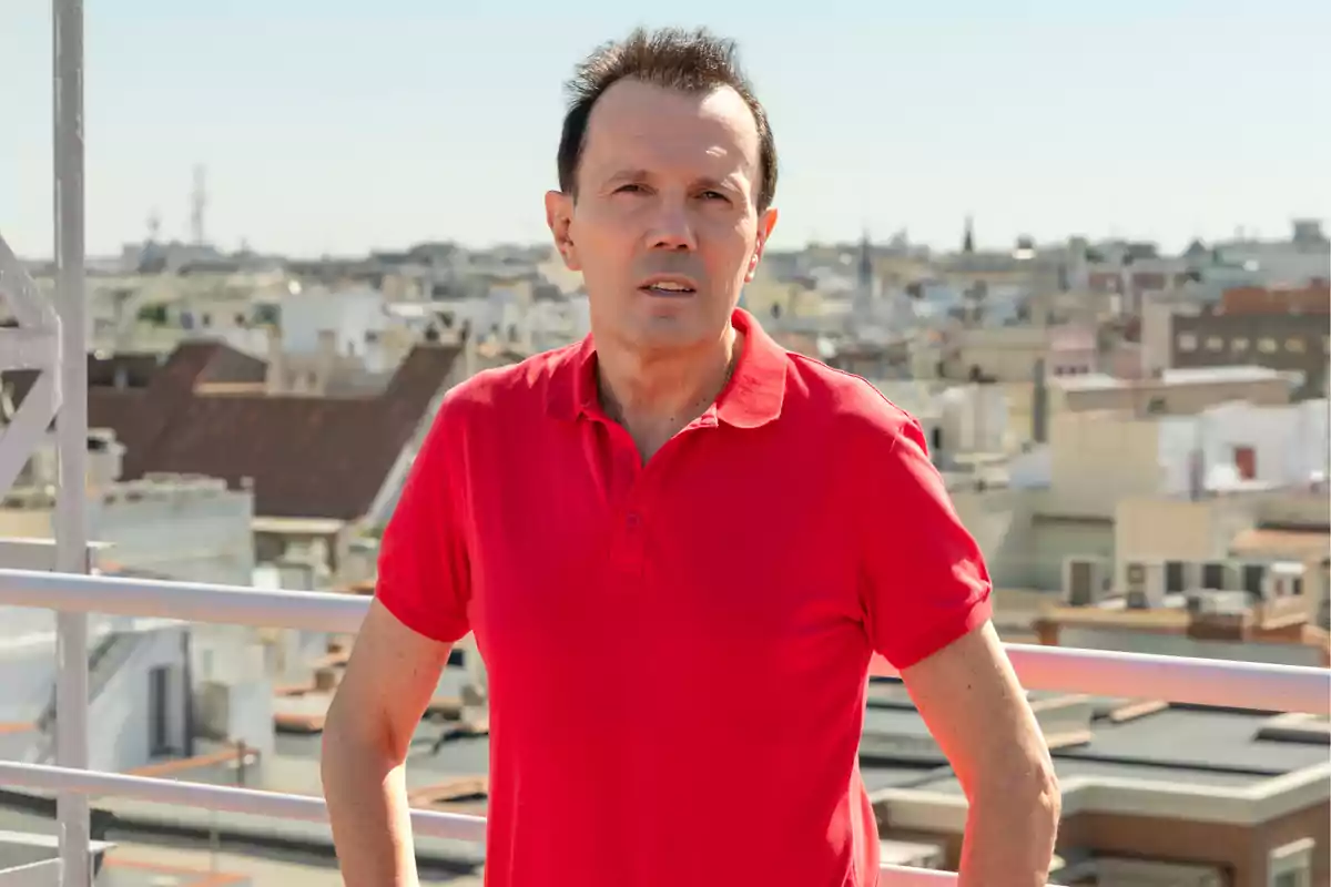 Hombre con camisa roja de pie en una azotea con una ciudad al fondo Hombre con camisa roja de pie en una azotea con una ciudad al fondo