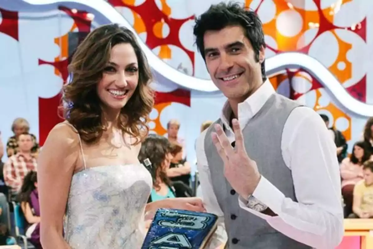 Dos presentadores sonríen en un set de televisión colorido con público al fondo Dos presentadores sonríen en un set de televisión colorido con público al fondo
