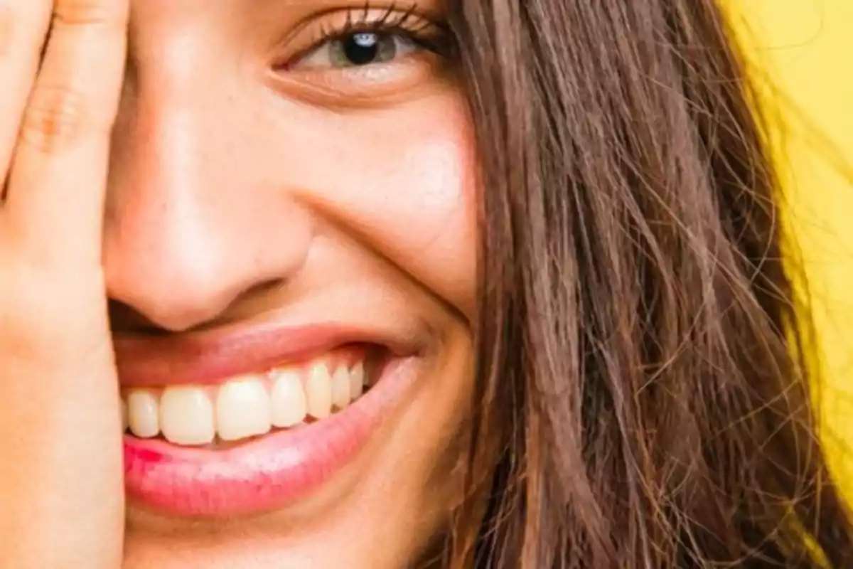 Mujer sonriendo cubriéndose un ojo con la mano sobre fondo amarillo