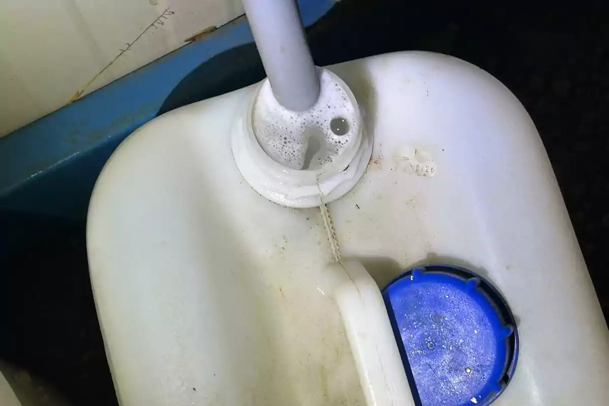 Contenedor de plástico blanco con tapa azul parcialmente desenroscada y una manguera introducida, generando espuma en la abertura Contenedor de plástico blanco con tapa azul parcialmente desenroscada y una manguera introducida, generando espuma en la abertura