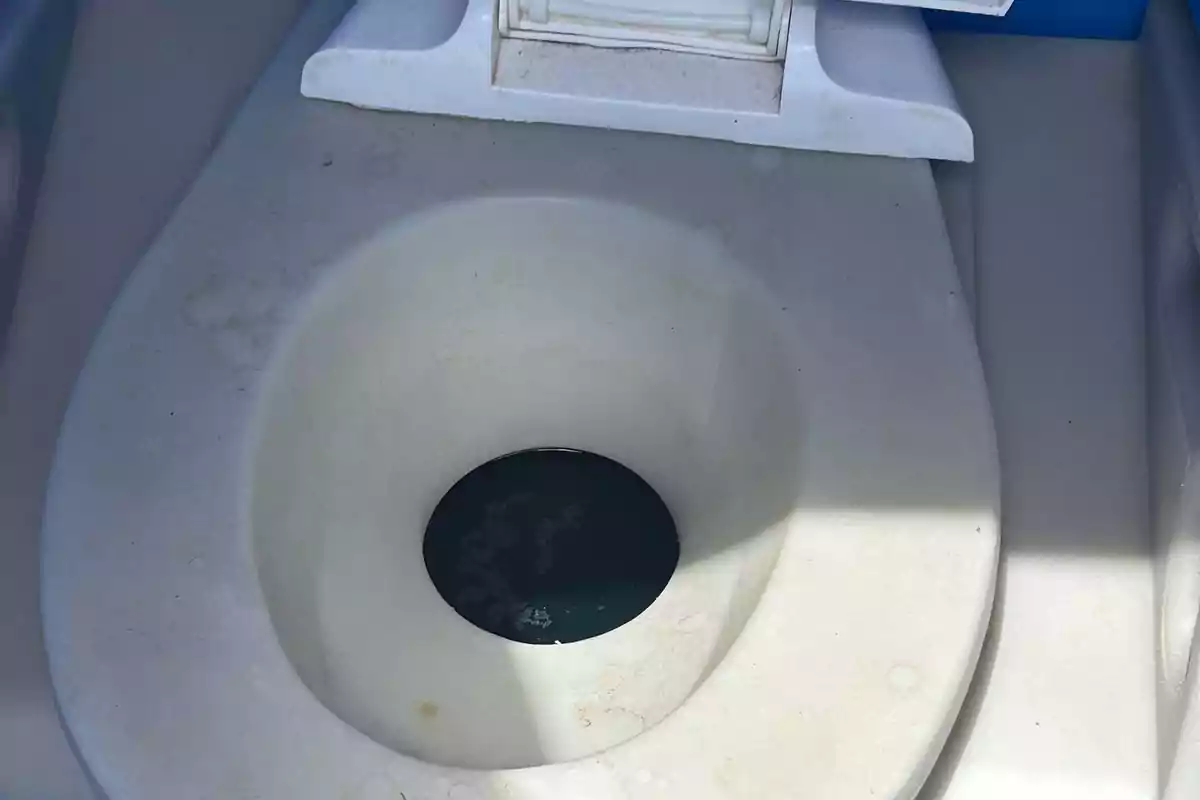 Inodoro portátil de plástico blanco con el interior parcialmente sombreado y agua azul en el fondo Inodoro portátil de plástico blanco con el interior parcialmente sombreado y agua azul en el fondo
