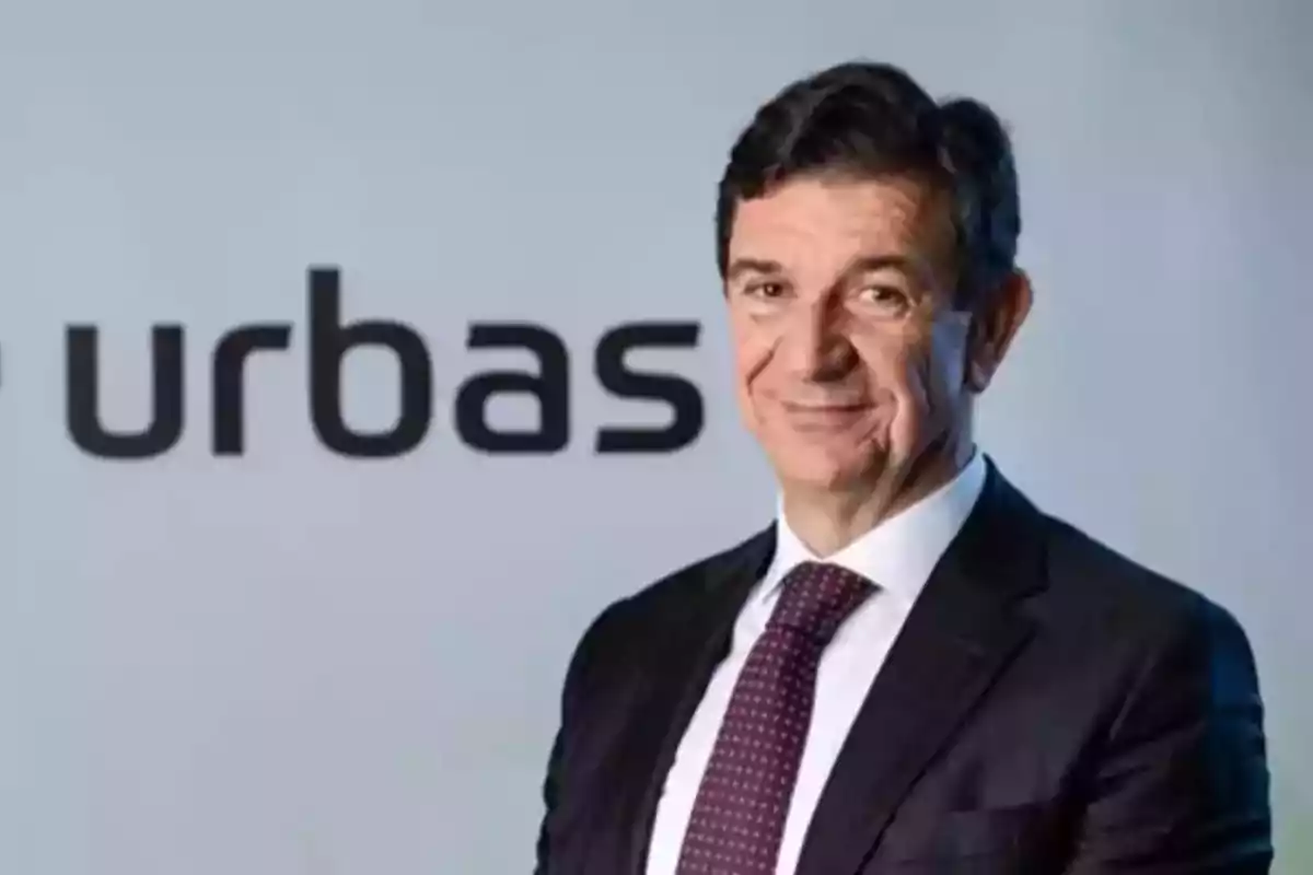 Hombre de traje y corbata posando frente a un fondo con el logo de la empresa Urbas