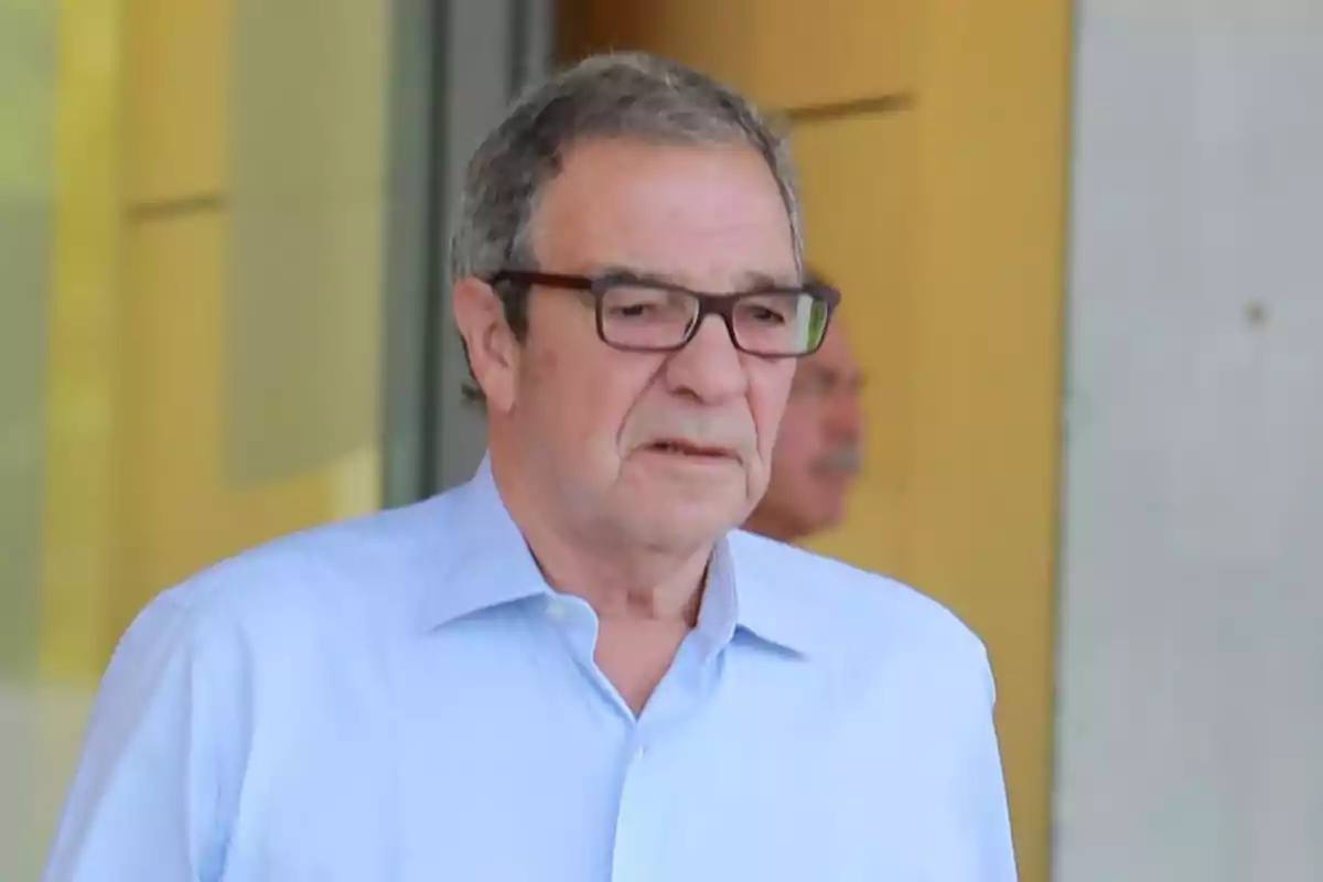 Hombre mayor con gafas y camisa azul claro caminando frente a un edificio Hombre mayor con gafas y camisa azul claro caminando frente a un edificio