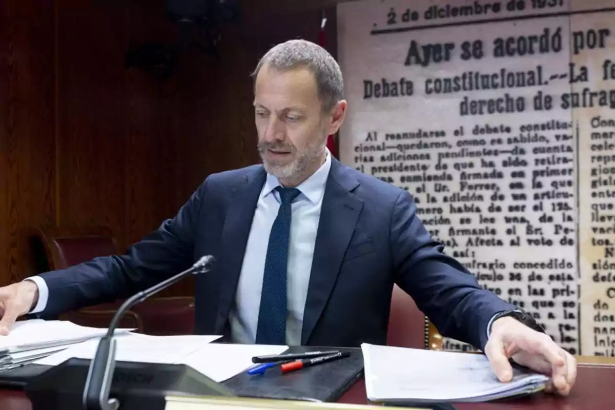 Hombre de traje sentado en una mesa revisando documentos con un fondo de periódico antiguo Hombre de traje sentado en una mesa revisando documentos con un fondo de periódico antiguo