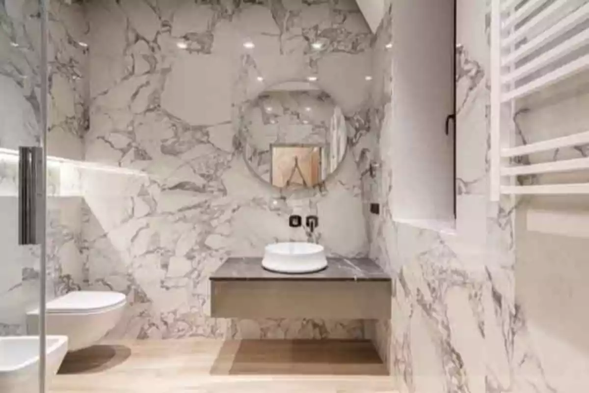 Baño moderno con paredes de mármol blanco, lavabo redondo sobre una encimera flotante y espejo circular grande