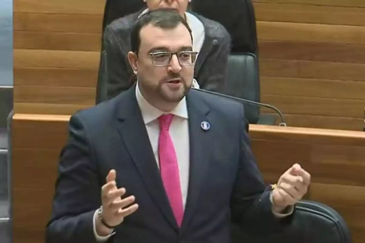 Hombre con gafas y corbata rosa hablando en un parlamento Hombre con gafas y corbata rosa hablando en un parlamento
