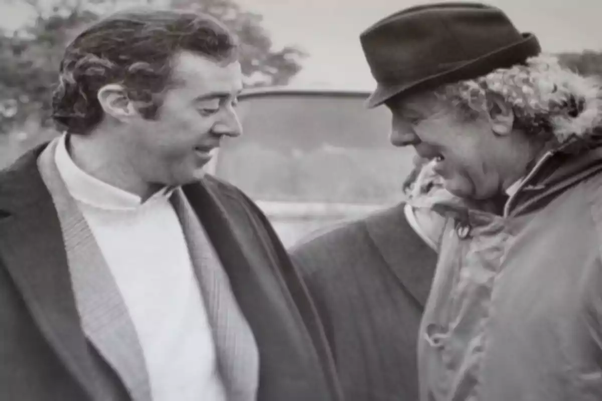 Dos hombres conversan y sonríen en una imagen en blanco y negro Dos hombres conversan y sonríen en una imagen en blanco y negro