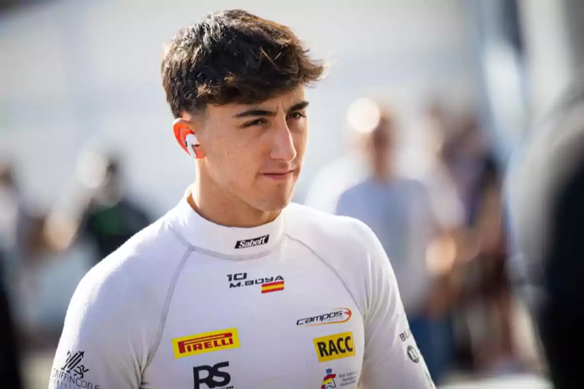Joven piloto de automovilismo con uniforme blanco y auriculares de color rojo y blanco en un ambiente de paddock de carreras