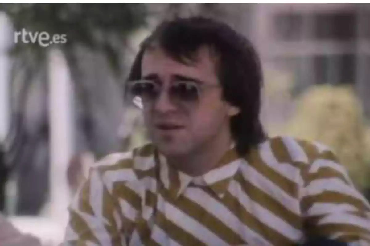 Hombre con gafas de sol y camisa de rayas blancas y amarillas sentado al aire libre Hombre con gafas de sol y camisa de rayas blancas y amarillas sentado al aire libre