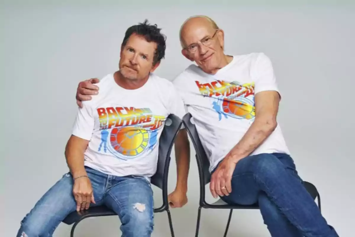 Dos hombres sentados juntos usando camisetas blancas con el logo de Back to the Future y jeans azules Dos hombres sentados juntos usando camisetas blancas con el logo de Back to the Future y jeans azules