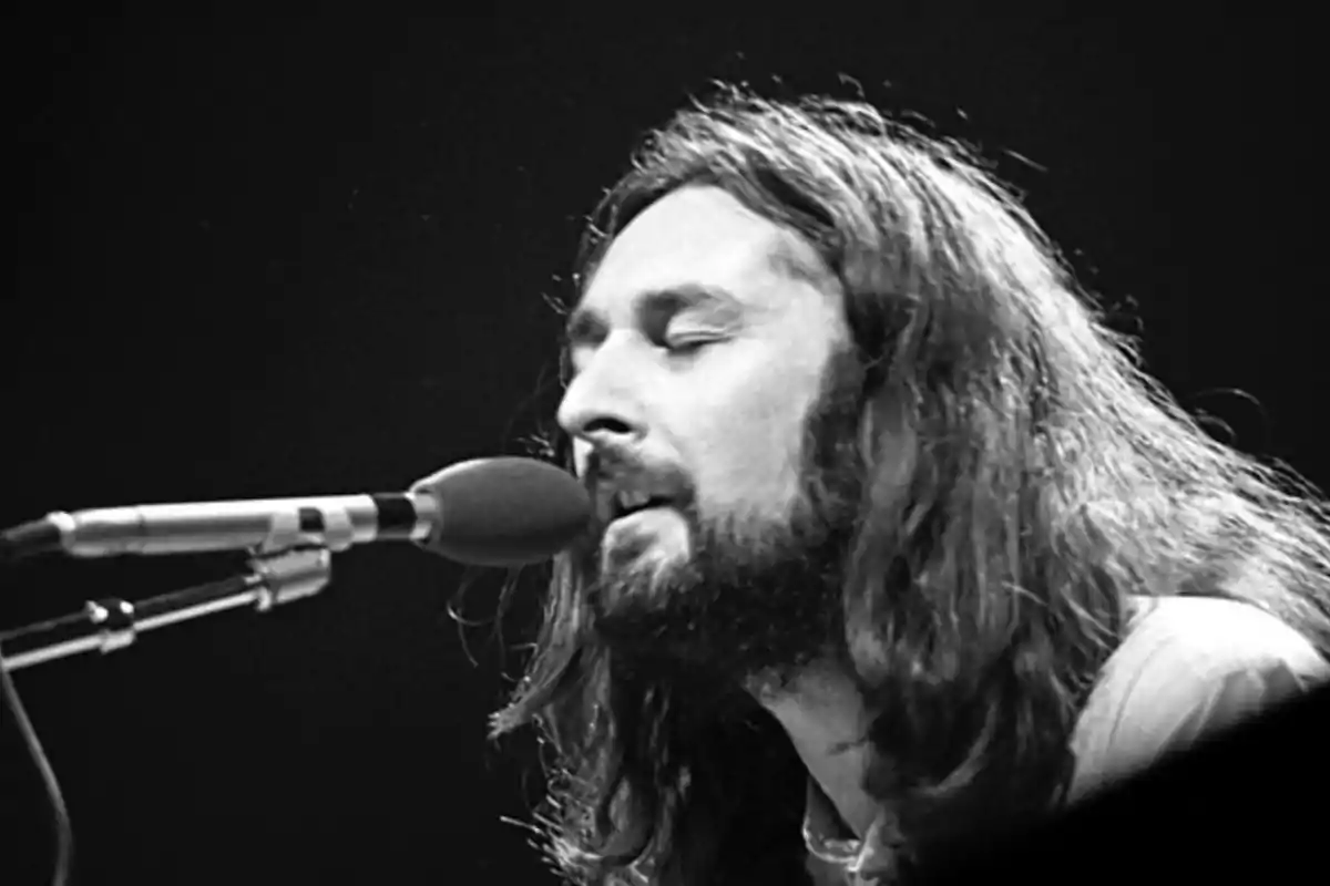 Hombre con barba y cabello largo cantando frente a un micrófono en blanco y negro