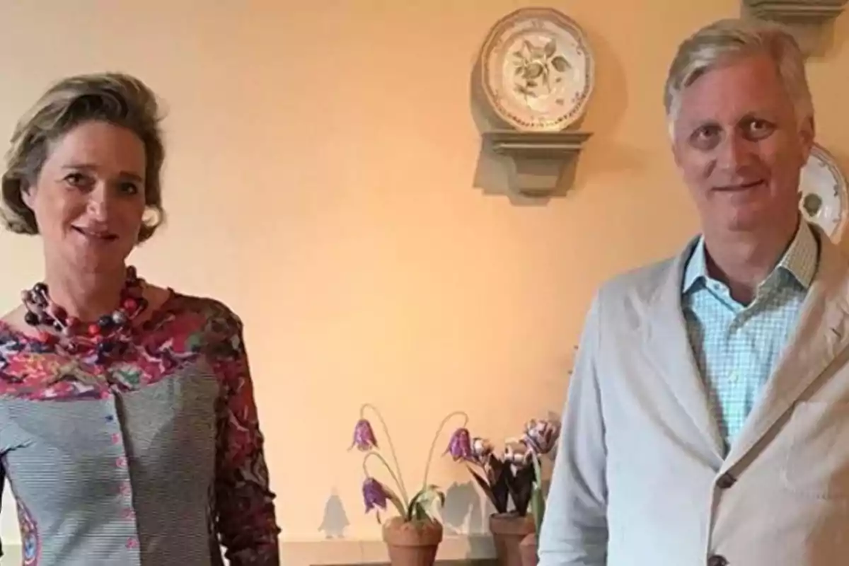 Una mujer y un hombre posan juntos en una habitación decorada con platos en la pared y macetas con flores sobre una repisa. Una mujer y un hombre posan juntos en una habitación decorada con platos en la pared y macetas con flores sobre una repisa.