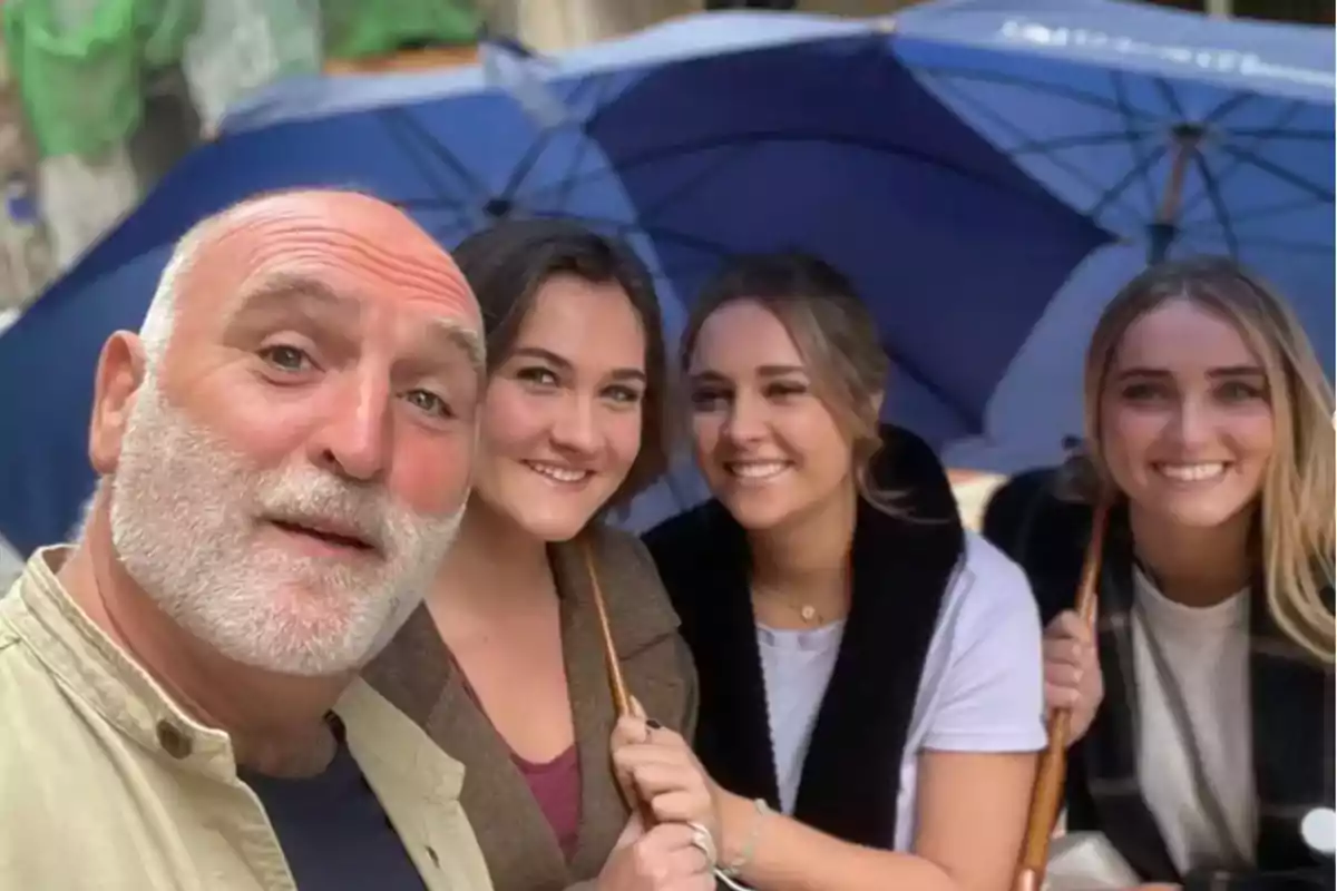 Un hombre y tres mujeres sonríen mientras posan para una selfie bajo paraguas azules en un día nublado. Un hombre y tres mujeres sonríen mientras posan para una selfie bajo paraguas azules en un día nublado.
