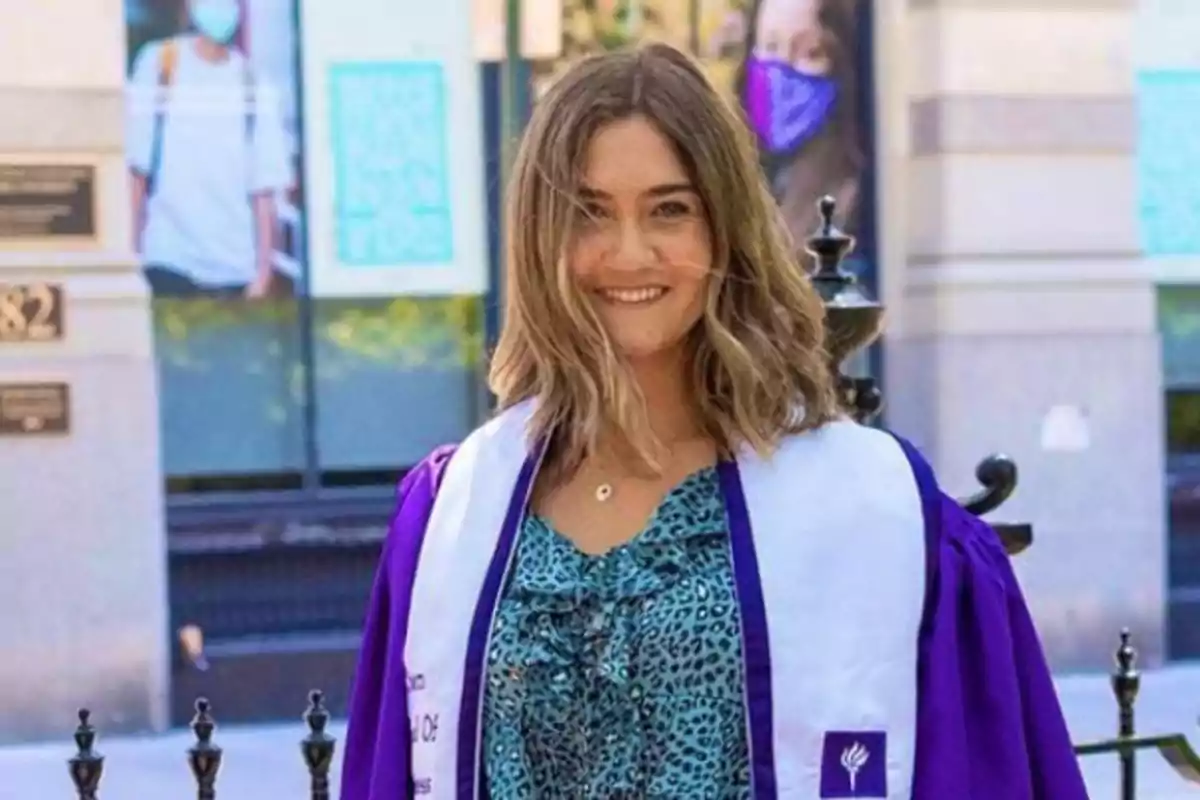 Joven con bata y estola de graduación sonríe al aire libre frente a un edificio Joven con bata y estola de graduación sonríe al aire libre frente a un edificio