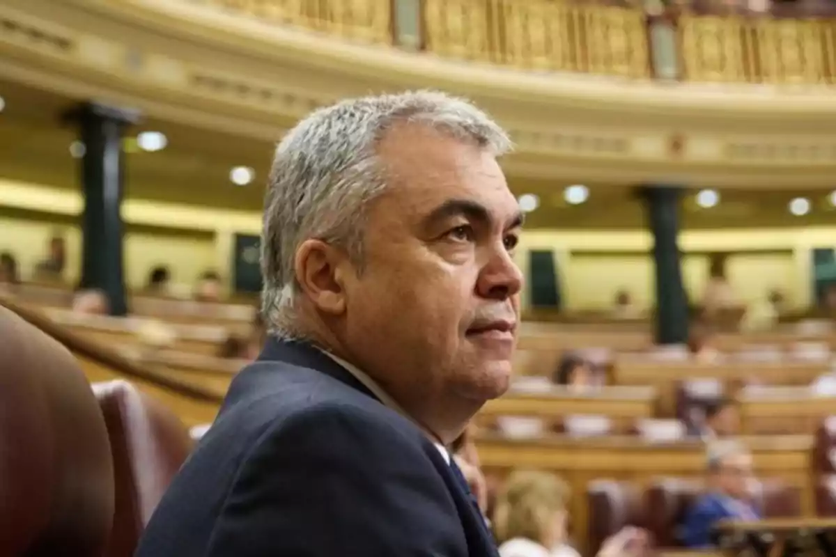Hombre de cabello canoso sentado en un recinto parlamentario con expresión seria Hombre de cabello canoso sentado en un recinto parlamentario con expresión seria