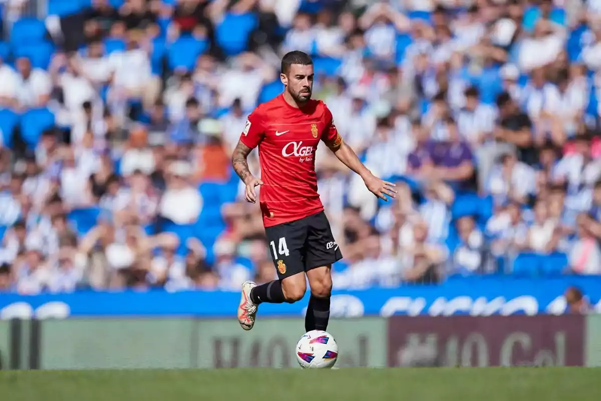 Futbolista con uniforme rojo y negro controlando el balón en un estadio lleno de espectadores Futbolista con uniforme rojo y negro controlando el balón en un estadio lleno de espectadores