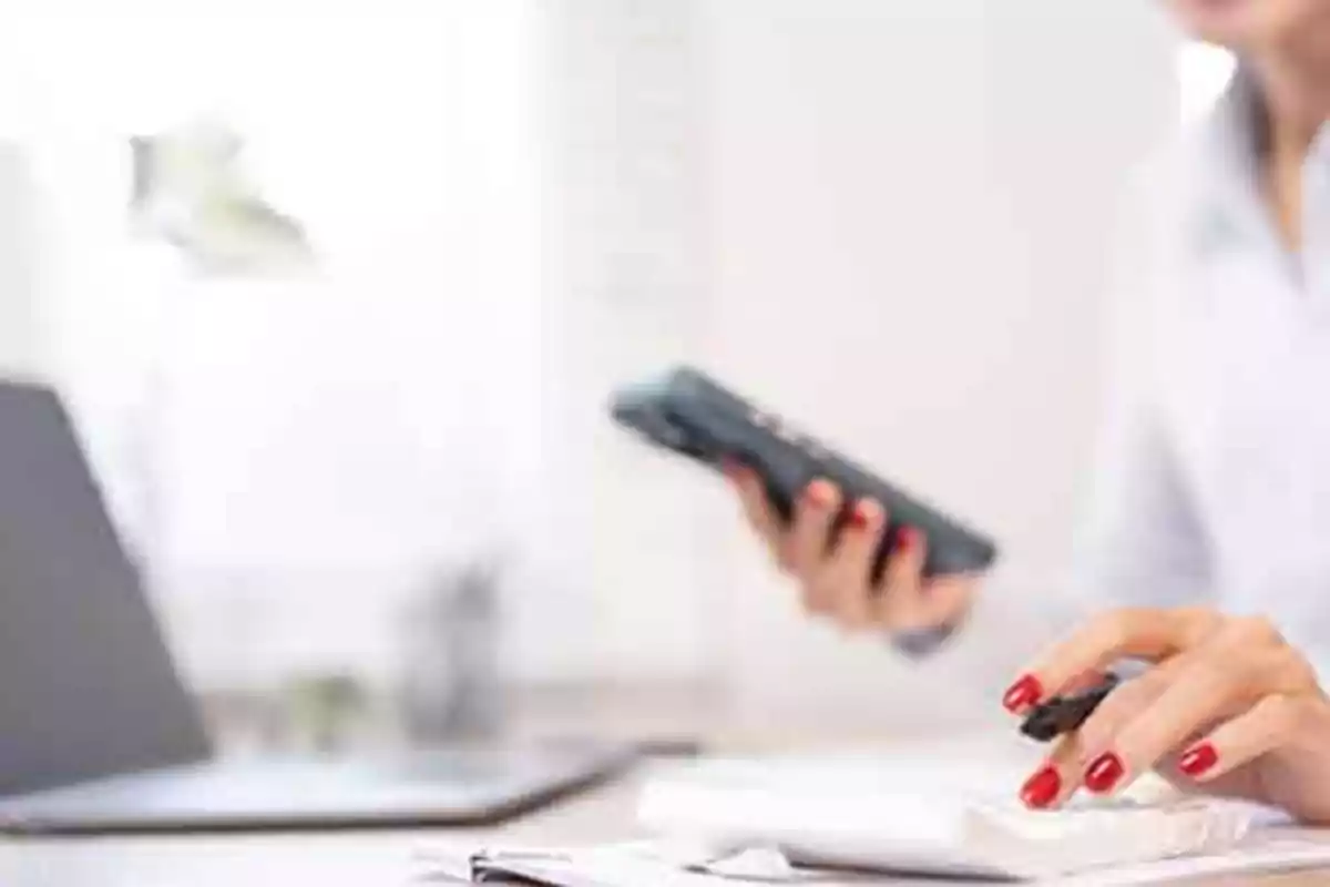 Persona usando una calculadora y sosteniendo un teléfono móvil en una oficina