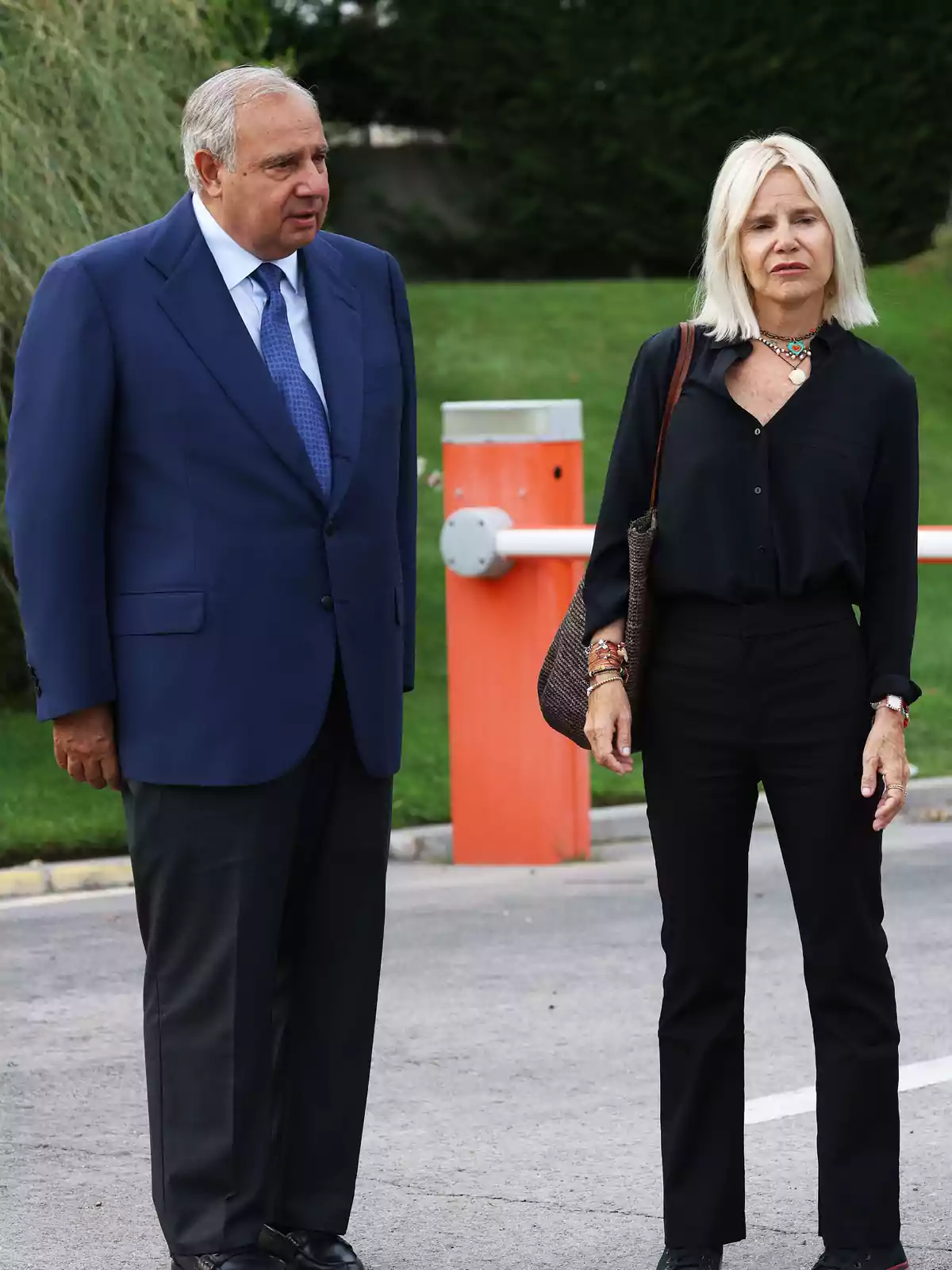 Un hombre con traje azul y una mujer vestida de negro están de pie al aire libre junto a una barrera de seguridad naranja Un hombre con traje azul y una mujer vestida de negro están de pie al aire libre junto a una barrera de seguridad naranja