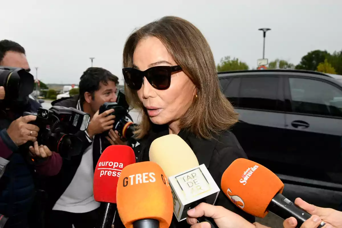 Mujer con gafas de sol rodeada de periodistas y varios micrófonos de diferentes medios de comunicación Mujer con gafas de sol rodeada de periodistas y varios micrófonos de diferentes medios de comunicación