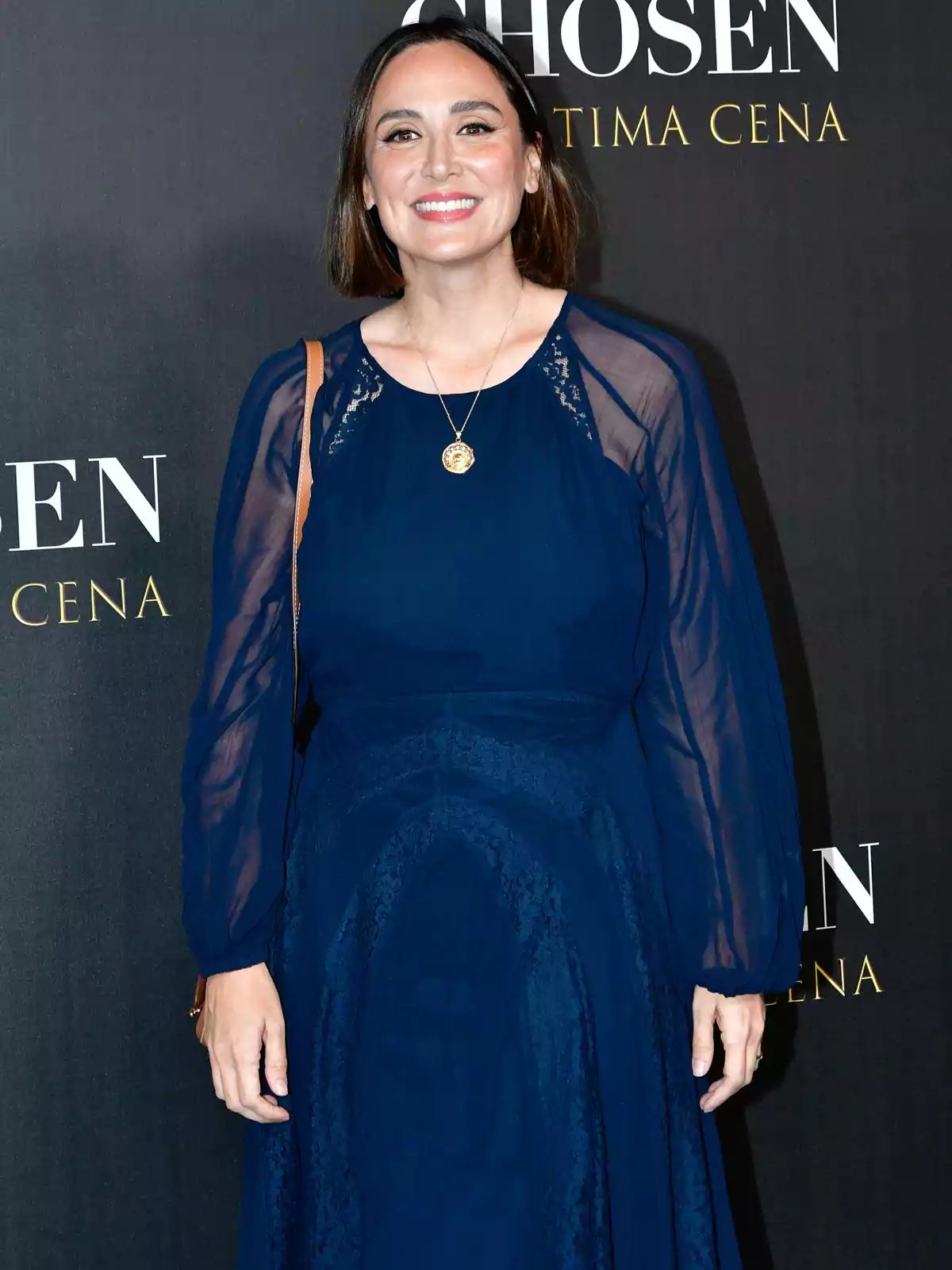 Mujer sonriendo vestida con un vestido azul oscuro de manga larga y fondo con letras doradas Mujer sonriendo vestida con un vestido azul oscuro de manga larga y fondo con letras doradas