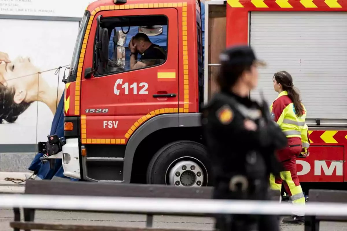 Un bombero dentro de un camión de bomberos parece preocupado mientras una policía y una trabajadora de emergencias están cerca del vehículo en una escena urbana Un bombero dentro de un camión de bomberos parece preocupado mientras una policía y una trabajadora de emergencias están cerca del vehículo en una escena urbana